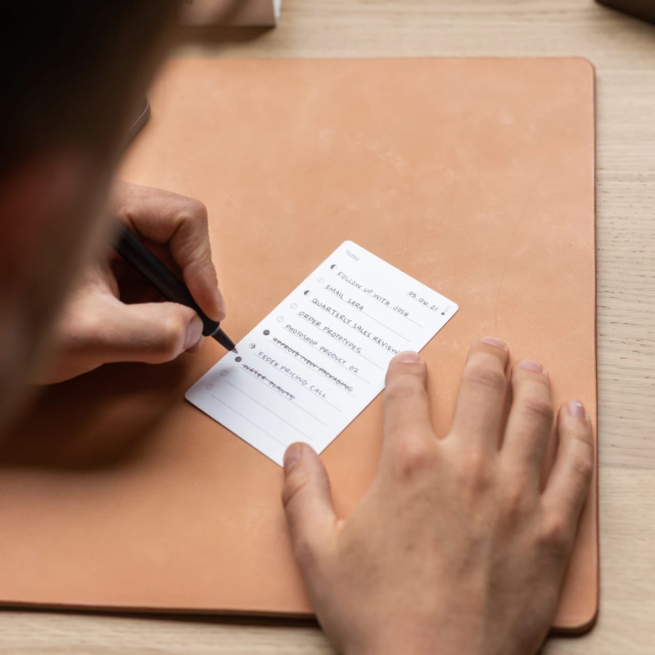 Person using a pen to cross a task off a productivity paper card.