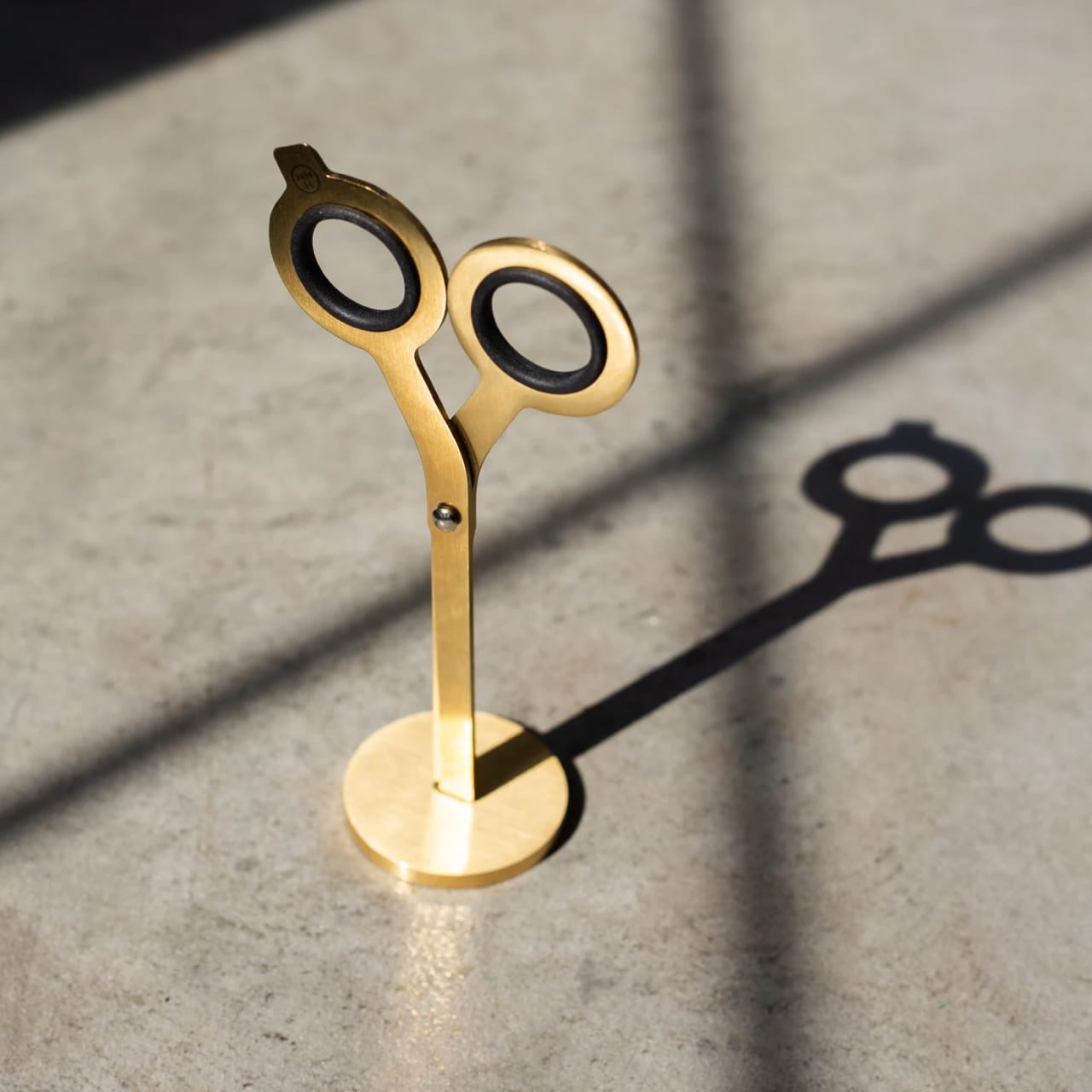 Brass scissors with geometric design, black steel finger holes, and included upright brass stand.