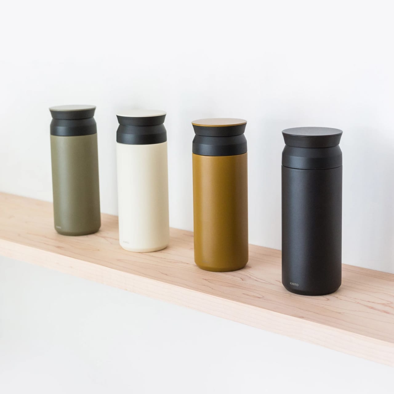 Collection of four insulated travel bottles on wooden shelf.